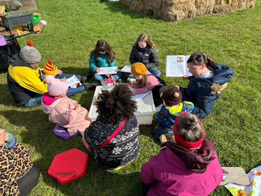 Children sitting on the grass around a low table doing a craft activity